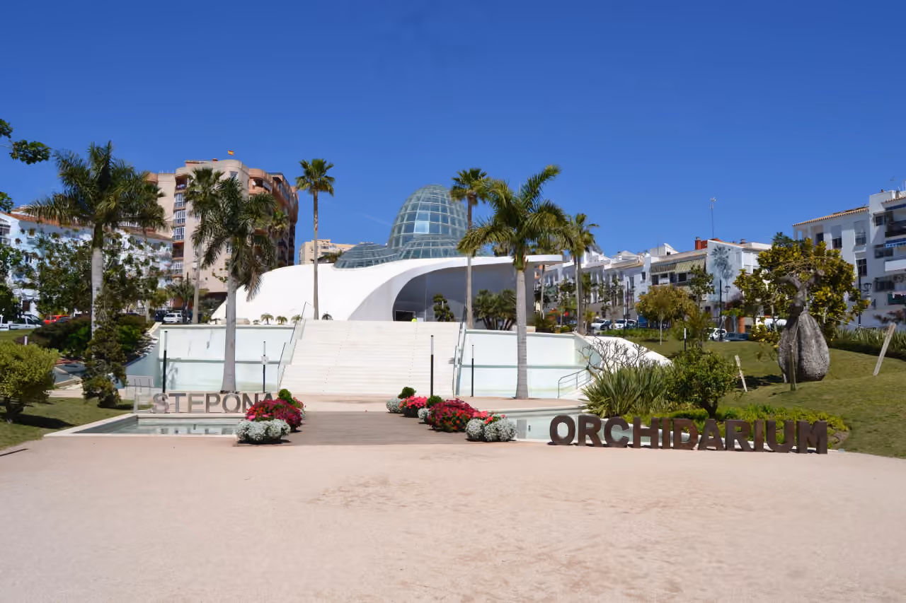 Környékfotó az Estepona Orchidarium külsejéről, a parkosított közterületi térről és a környező városképről a BOUGAINVILLEA ESTEPONA közelében