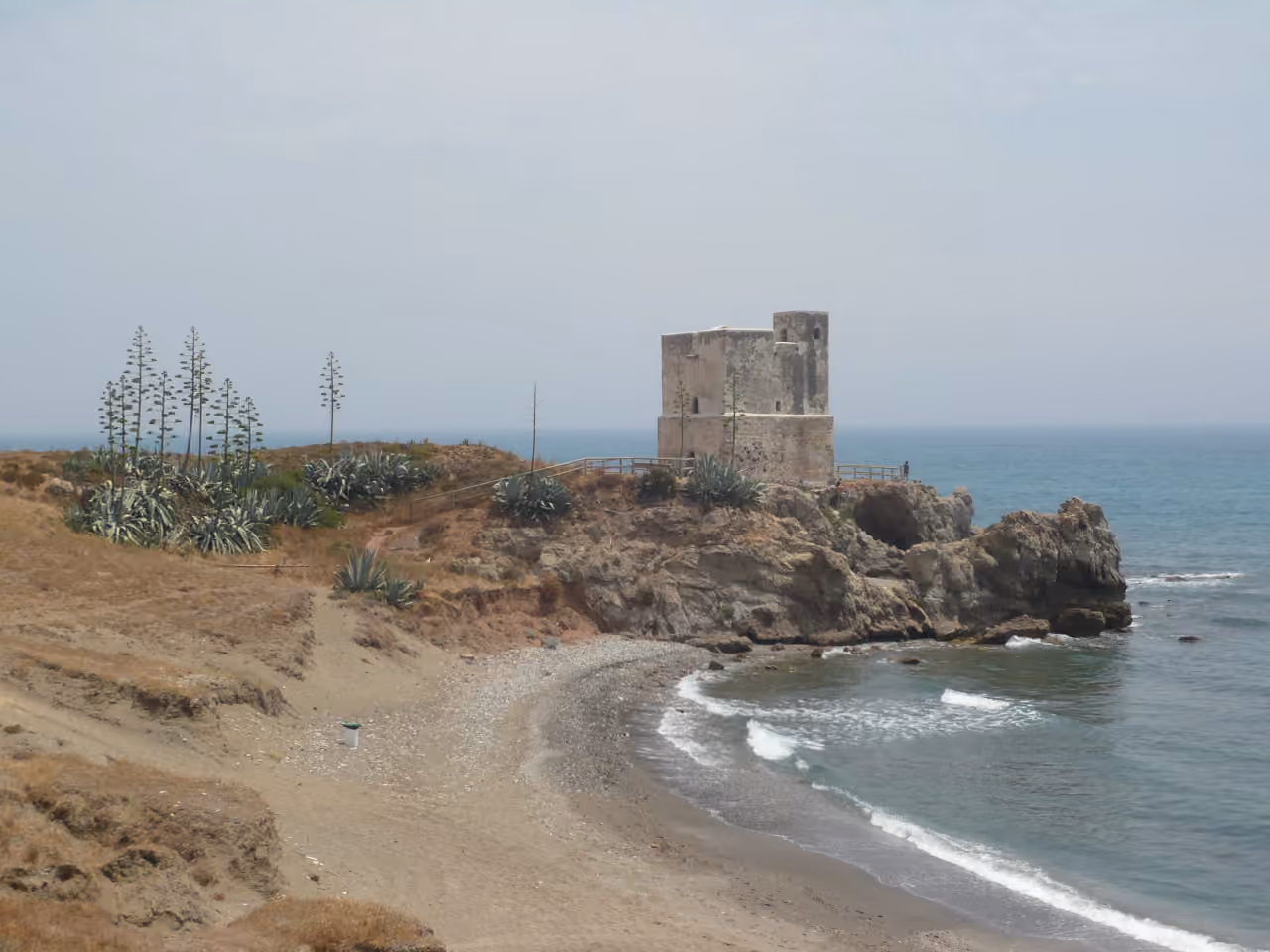 Zdjęcie okolicy AUREA VILLAS przedstawiające zabytkową nadbrzeżną wieżę strażniczą (Torre de Bahía de Casares) na skalistym cyplu przy wybrzeżu Morza Śródziemnego w Casares, Málaga, Hiszpania.