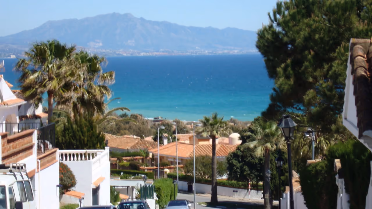 Områdesbild vid AMPHORA BEACH FASE IV med Medelhavskust, palmer, villor med terrakottatak, turkost hav och avlägsna berg nära Manilva, Costa del Sol