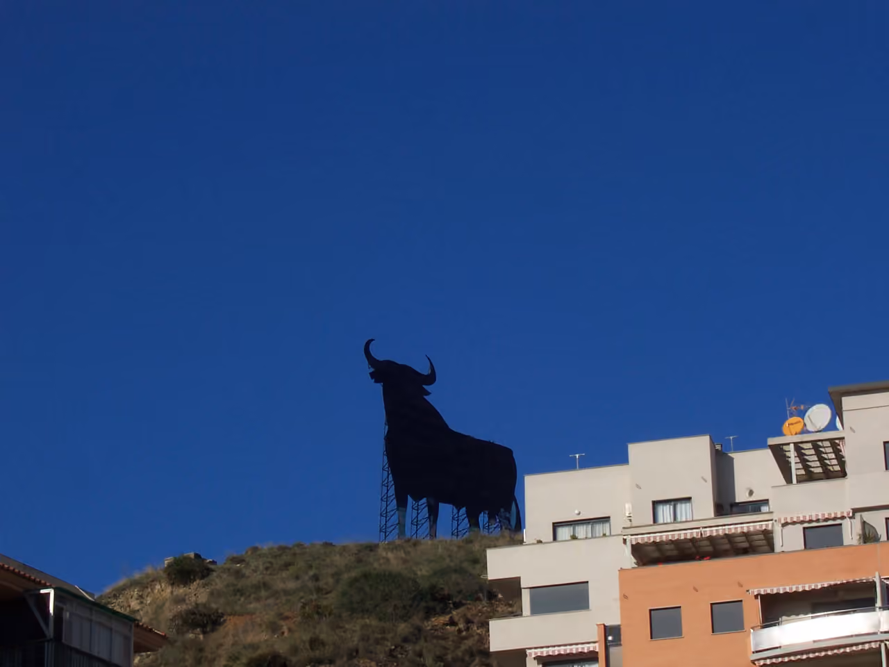 Områdebilde nær TORRE BIZNAGA av Osborne-tyren i åssiden over Fuengirola, med boligbygg og klar blå himmel