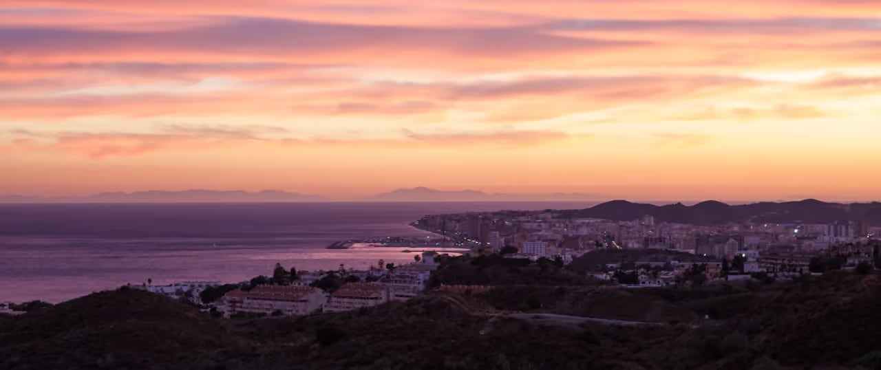 Photographie des environs de BELVEDERE COLLECTION : vue panoramique au coucher du soleil sur Fuengirola, le littoral, le port et la mer Méditerranée, avec les montagnes de l’Atlas à l’horizon